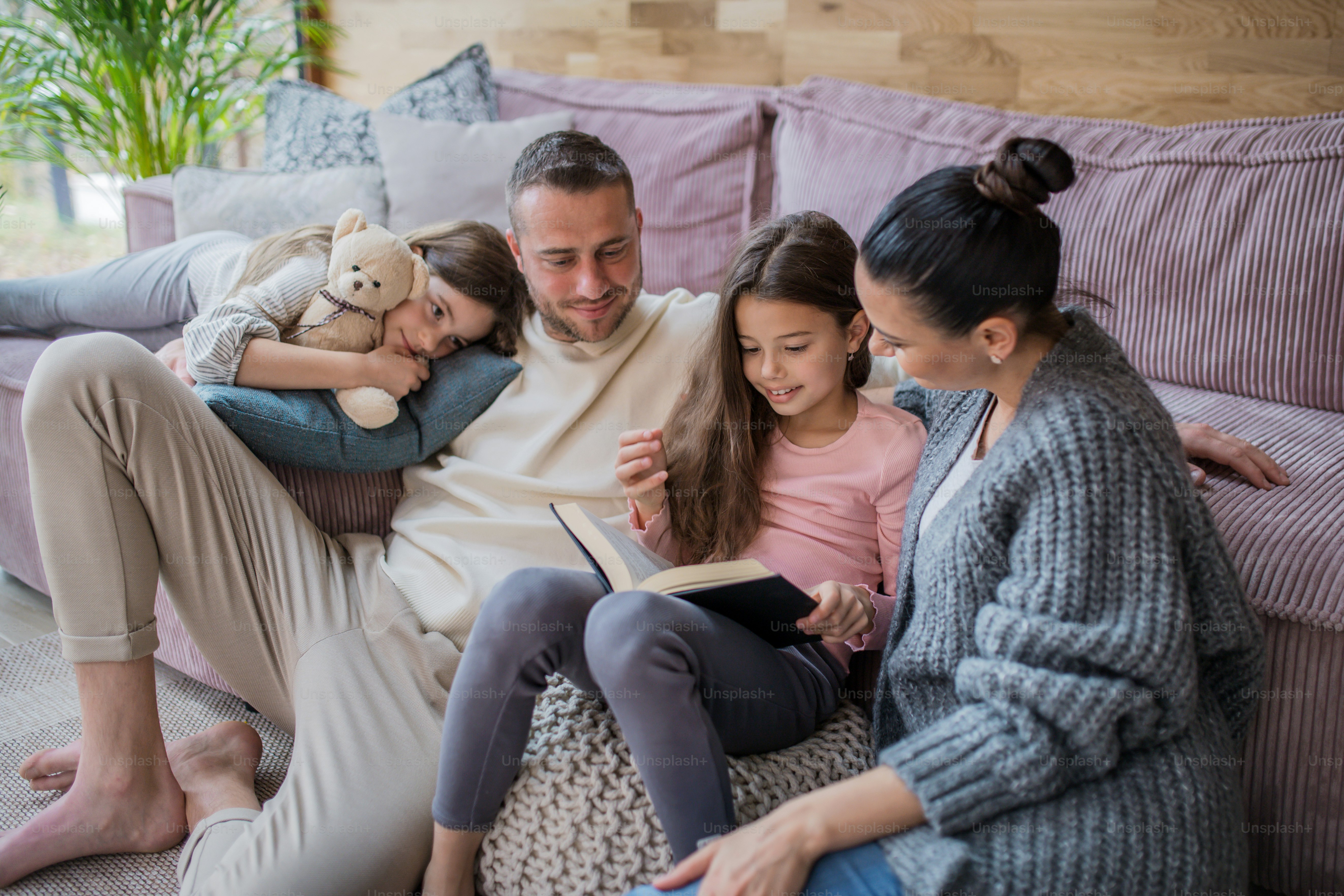 Dos hermanas felices con una madre y un padre sentados en el suelo abrazándose y leyendo un libro en casa