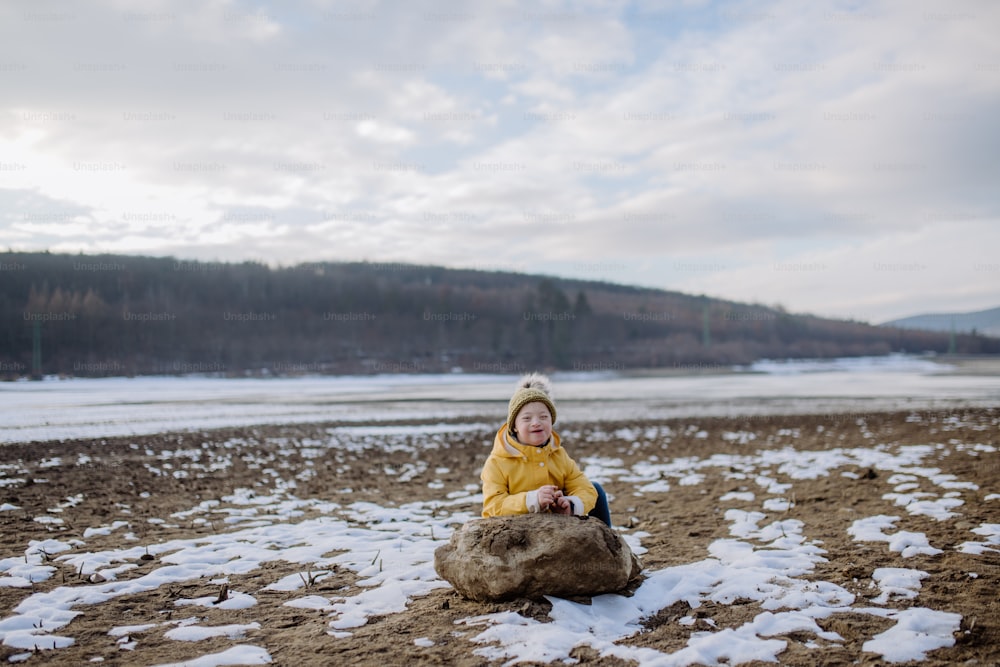 Un niño feliz con Down afuera junto al lago en invierno.