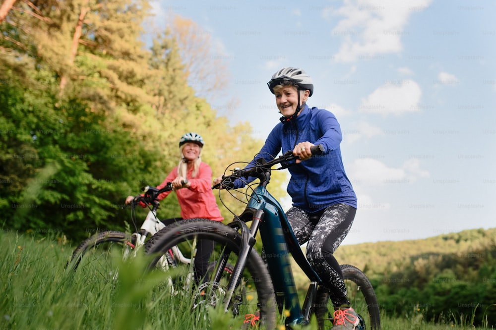Happy active senior women friends cycling together outdoors in nature in meadow.