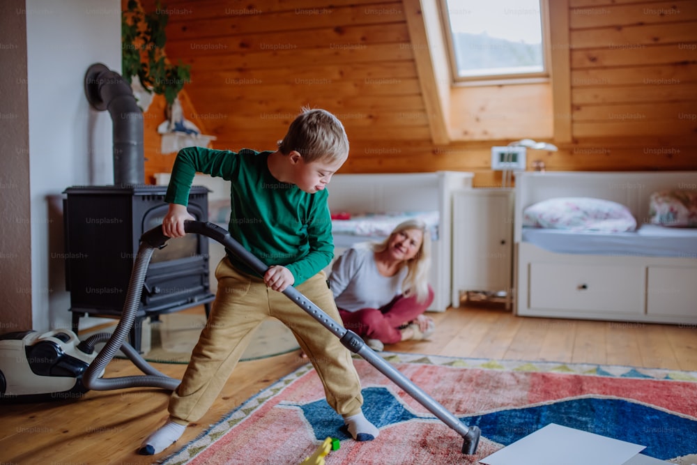 A boy with Down syndrome with his grandmother vacuum cleaning at home