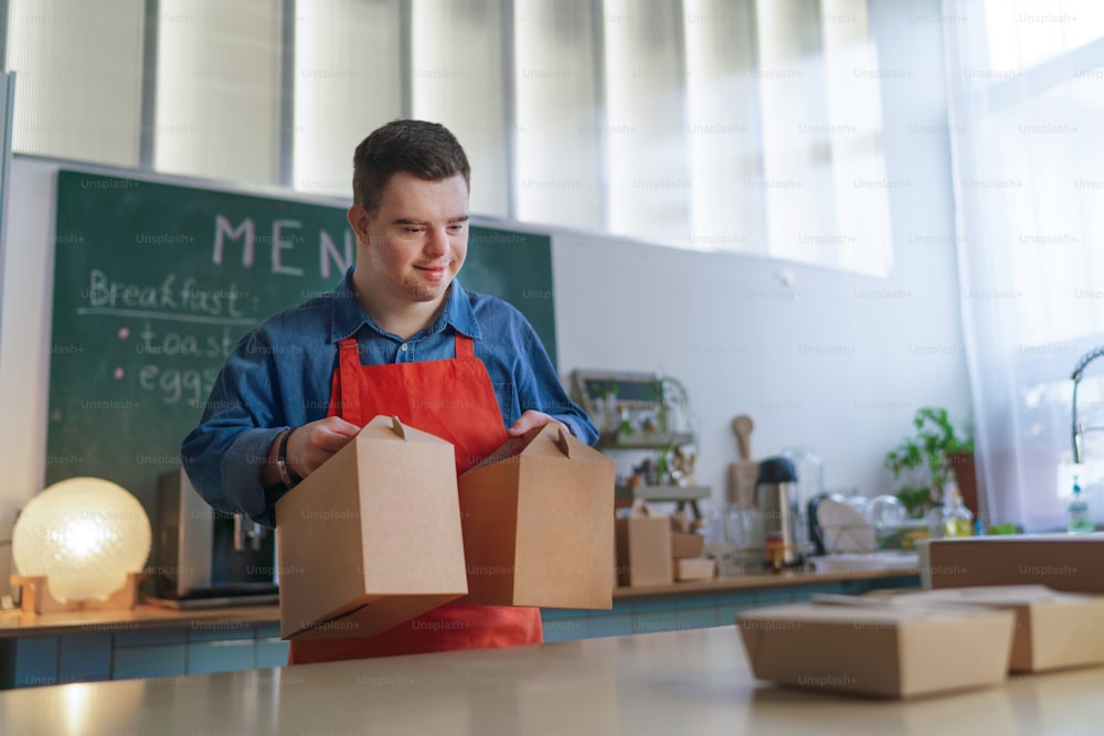 A cheerful young Down Syndrome waiter working in take away restaurant, social inclusion concept.