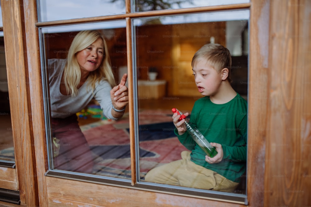 ダウン症の男の子と、母親と祖母が家の窓を掃除している。