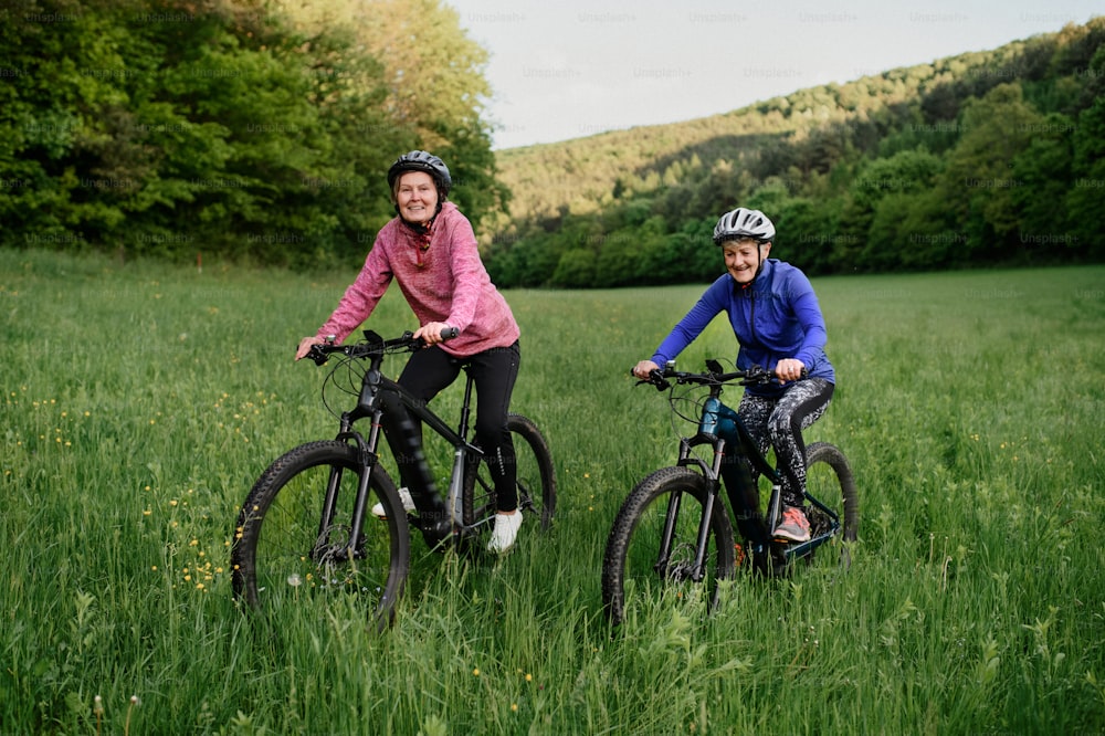 Happy active senior women friends cycling together outdoors in the nature.