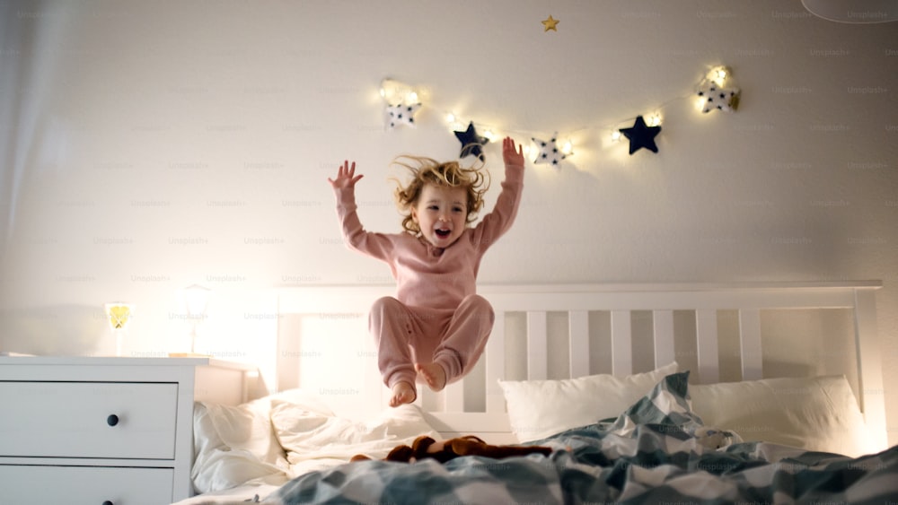 笑う2人の小さな子供が、自宅の室内のベッドに飛び乗って楽しんでいます。