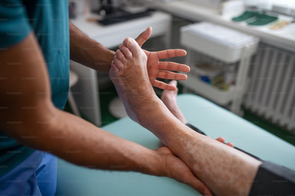 A close-up of physiotherapist exercising with senior patient's leg in a physic room.
