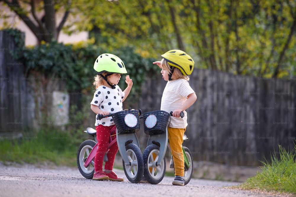 Happy small children boy and girl with helmets and balance bikes outdoors playing.