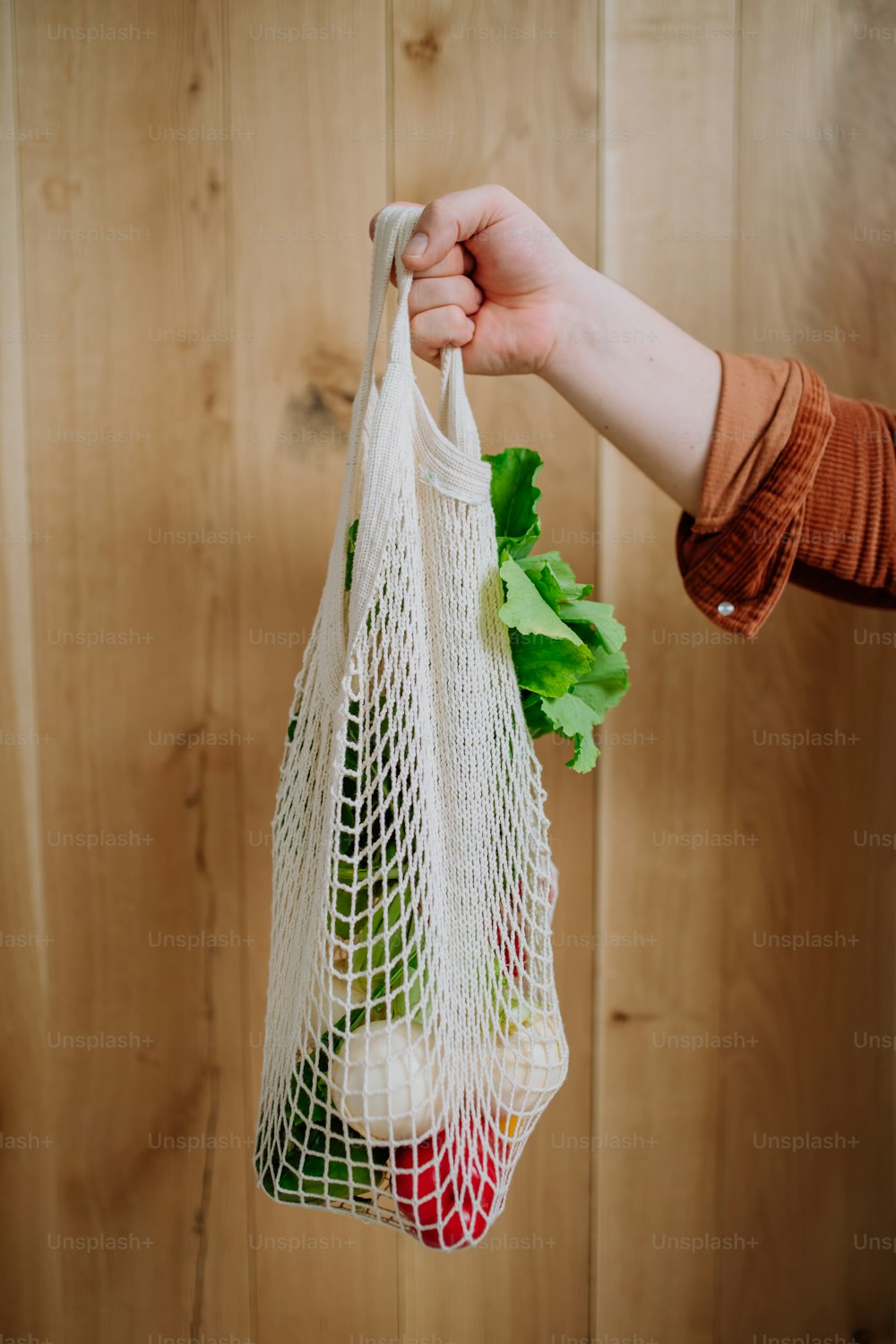 A woman holding a reusable mesh bag with fresh vegetables. Zero waste concept.