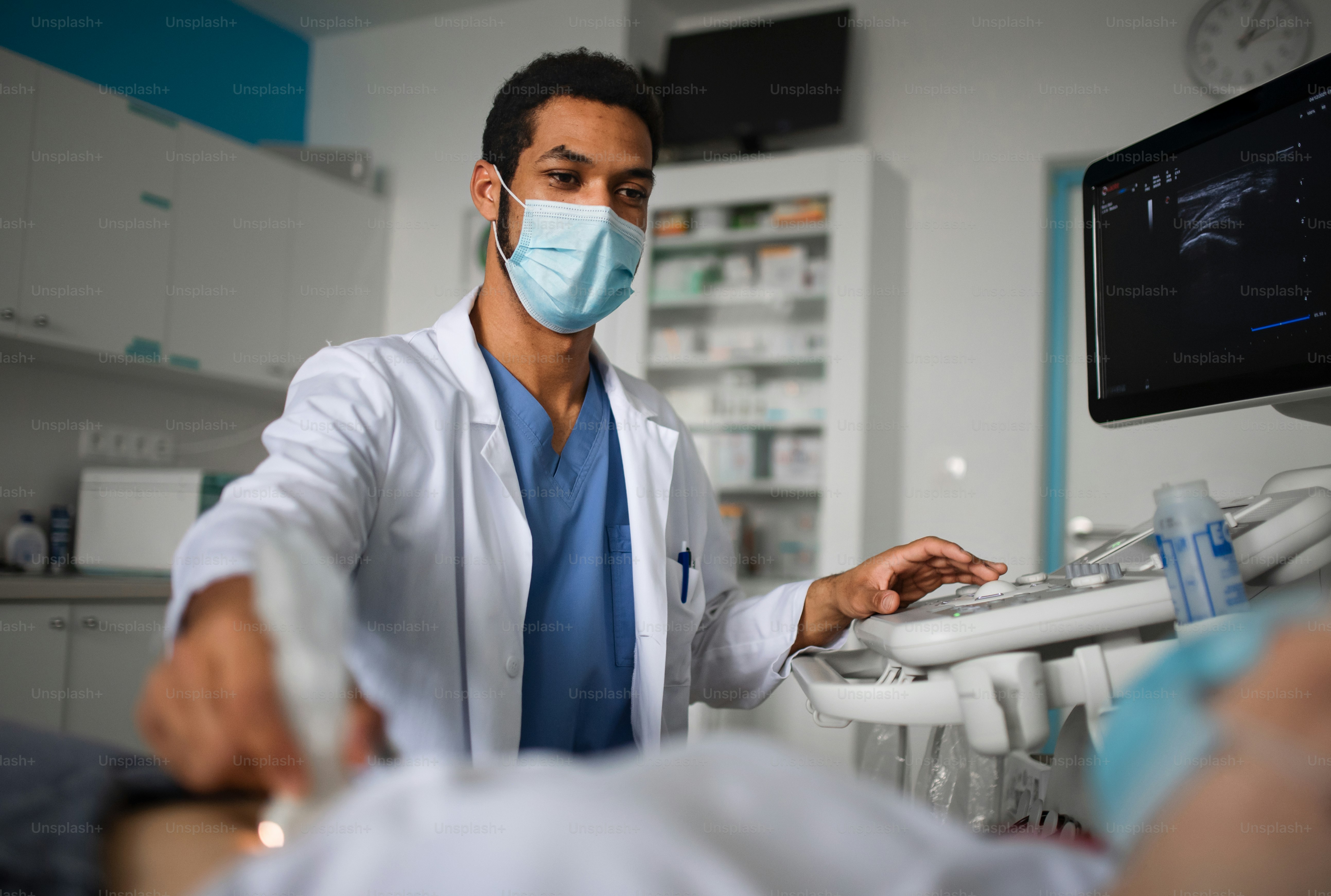 Ein junger Arzt untersucht Patienten mit einem Ultraschallgerät in der Klinik, Coronavirus-Konzept.