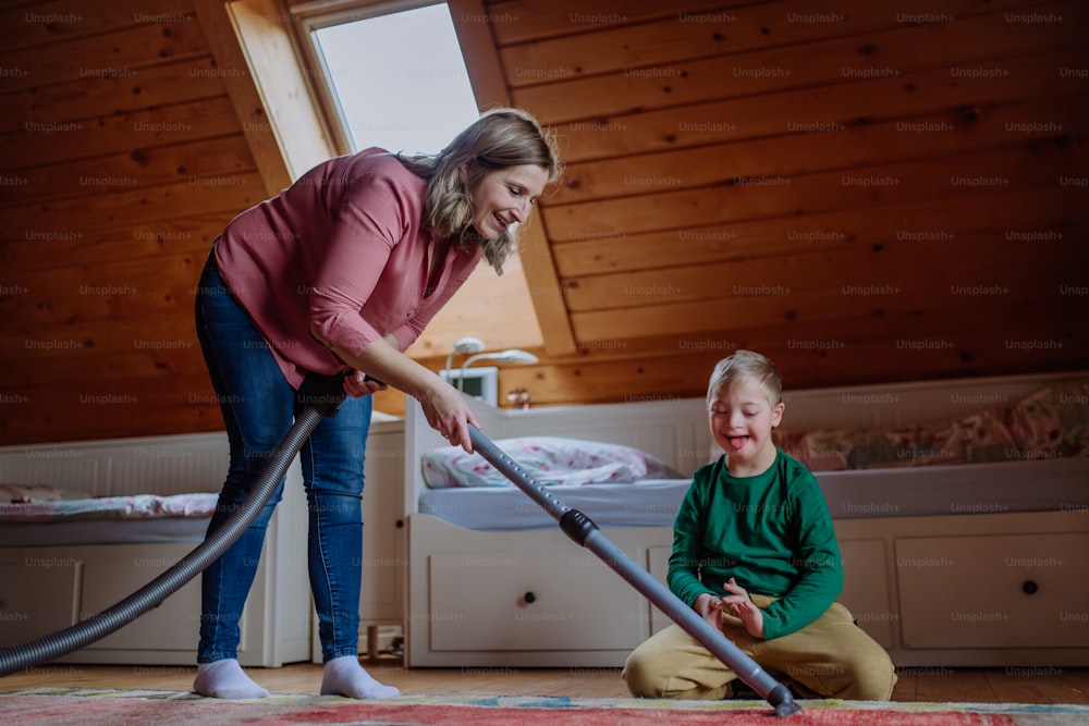 Um menino com síndrome de Down com sua mãe limpando a vácuo em casa