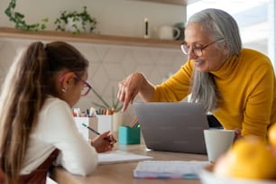 A small girl with senior grandmother doing homework at home.