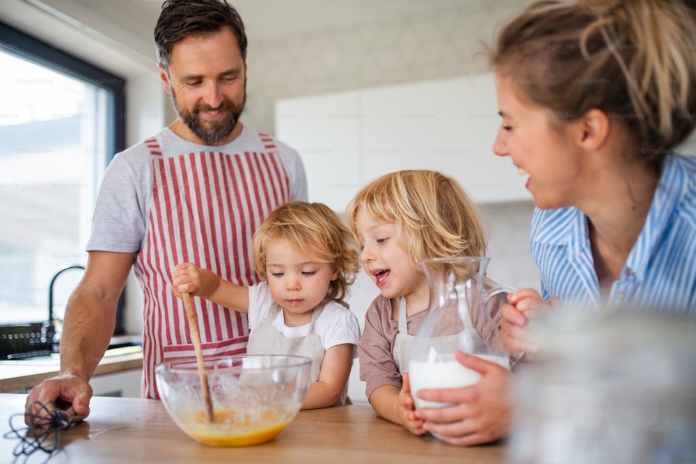 Vista frontale della giovane famiglia con due bambini piccoli all'interno in cucina, cucinando.