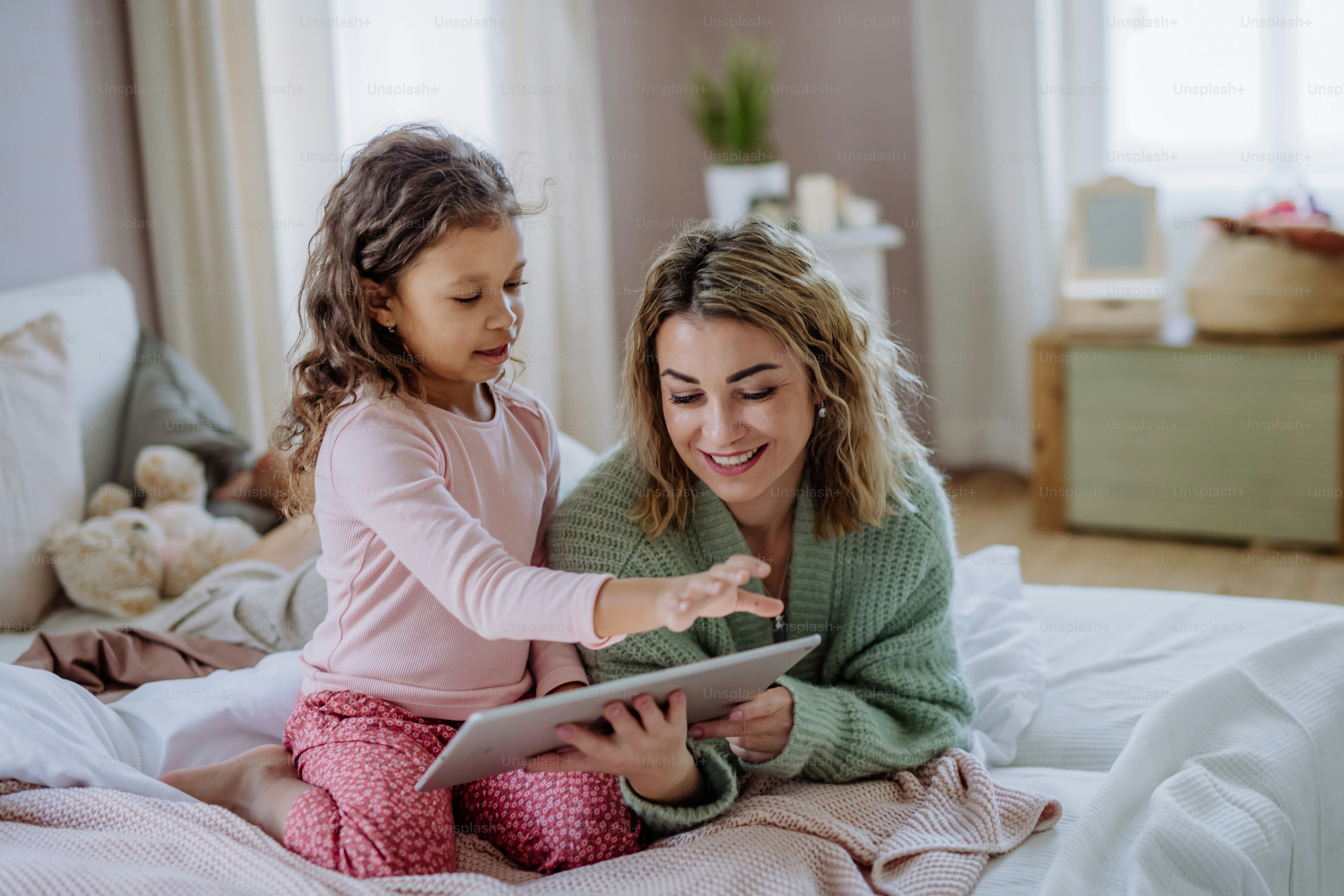 Una madre feliz con su hija pequeña acostada en la cama y usando la ...