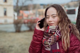 A young woman with Down syndrome walking in street in winter and using smartphone