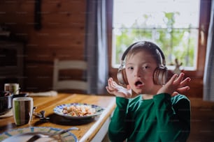 A boy with Down syndrome having lunch with headphones and looking at camera at home.