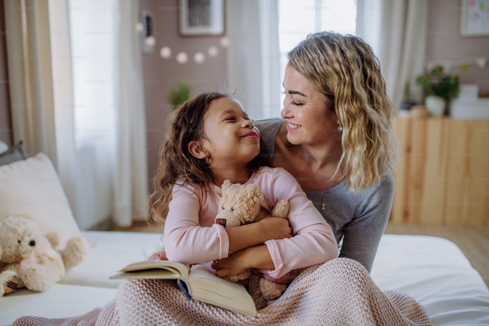 A happy mother hodling her little daughter and looking at each other in bed.