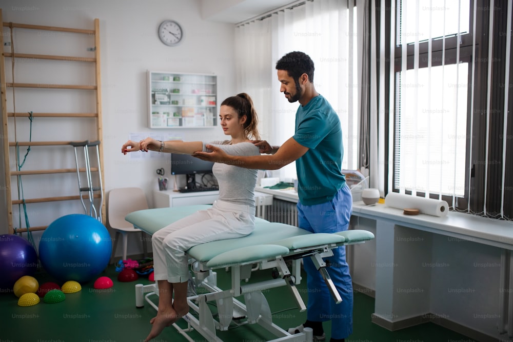 Un giovane fisioterapista maschio che esamina una giovane paziente donna in una stanza fisica