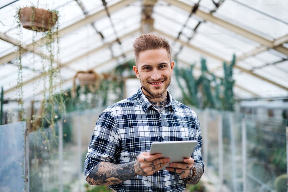 Man researcher with tablet standing in greenhouse in botanical garden, looking at camera.