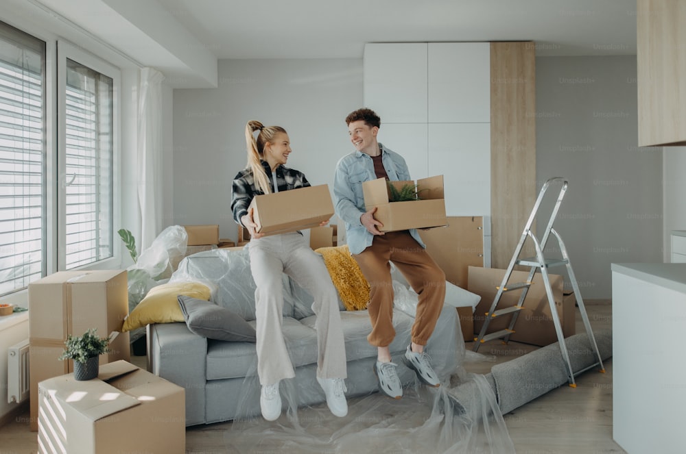 A cheerful young couple in their new apartment, carrying boxes. Conception of moving.