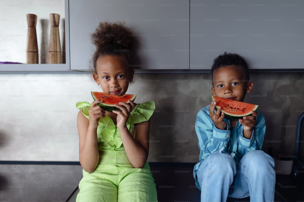 Niños multirraciales comiendo un melón en la cocina durante los días calurosos y soleados.