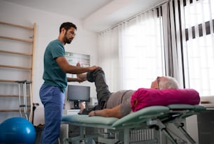 Un fisioterapista che si esercita con la gamba di un paziente anziano in una stanza fisica.
