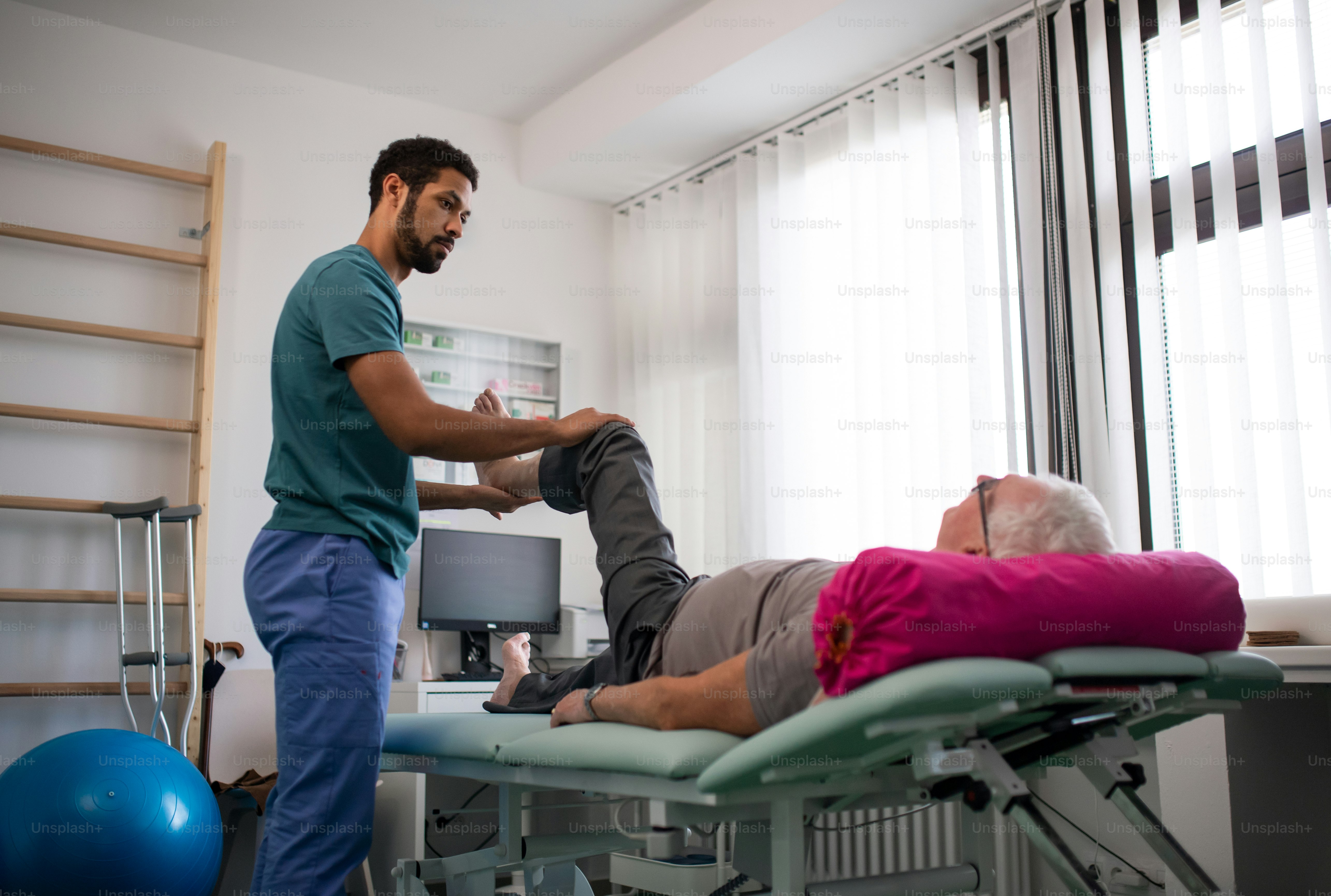 A physiotherapist exercising with senior patient's leg in a physic room