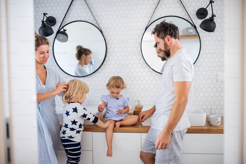 Une jeune famille avec deux jeunes enfants à l’intérieur dans la salle de bain, en train de parler.