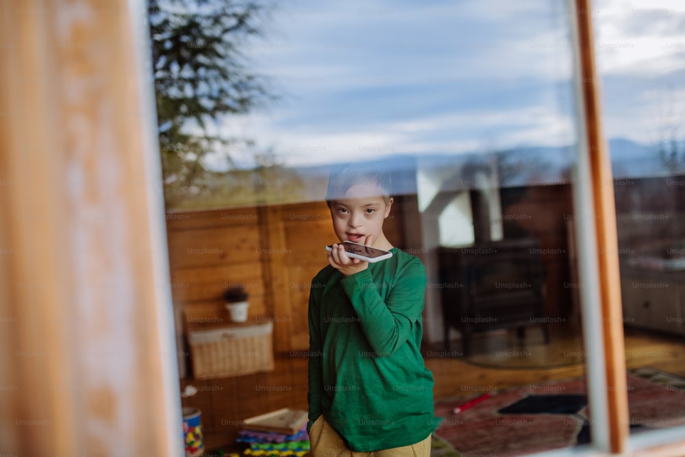 Un ragazzino triste con la sindrome di Down che usa lo smartphone a casa