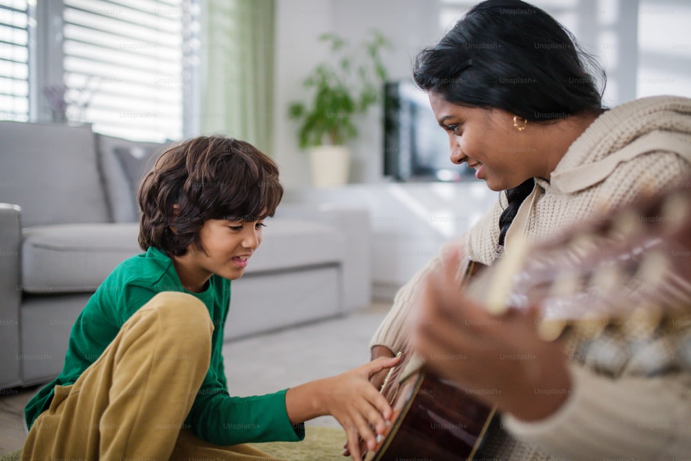 A little multiracial boy learning to play the guitar with his mother at home.