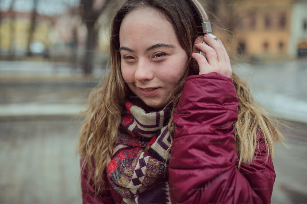 A happy young woman with Down syndrome listening to music in town in winter