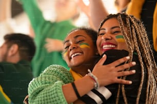Brazilian young sisters football fans celebrating their team's victory at a stadium.
