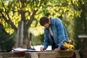 A handyman measuring a board, outside in garden.