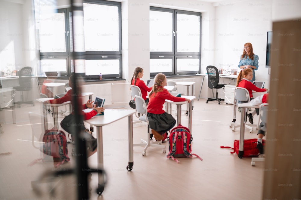 A rear view,class of pupils sitting and listening to teacher in classroom