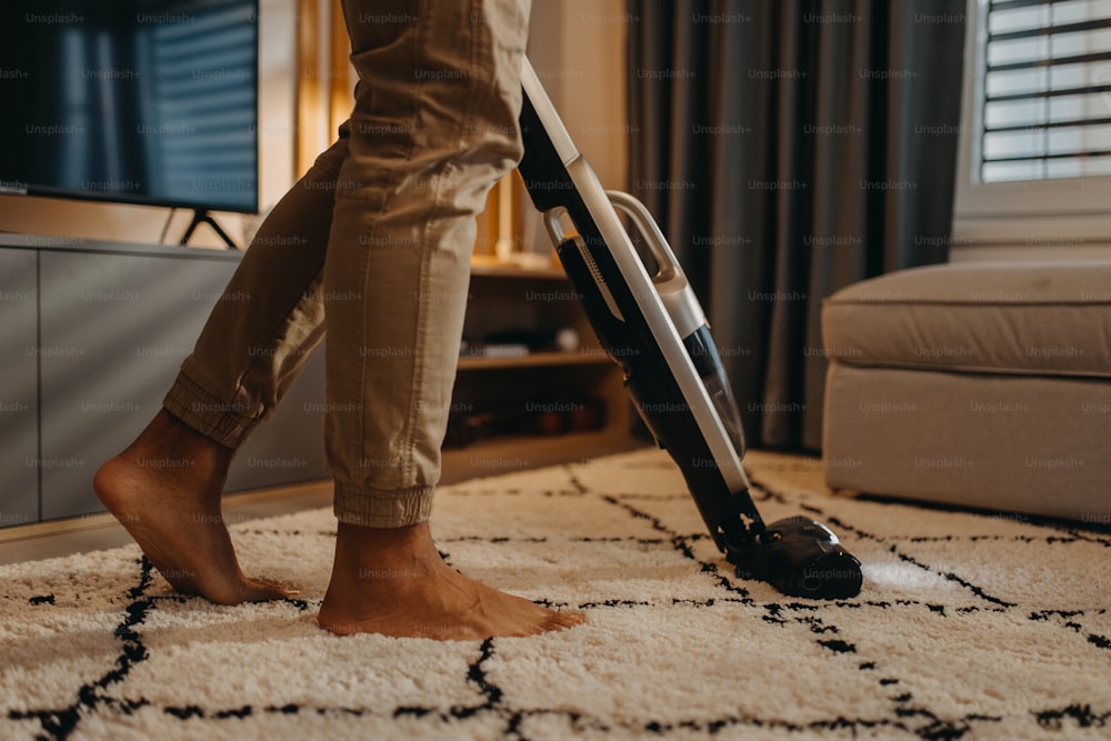 A lowsection of man hoovering carpet with vacuum cleaner in living room
