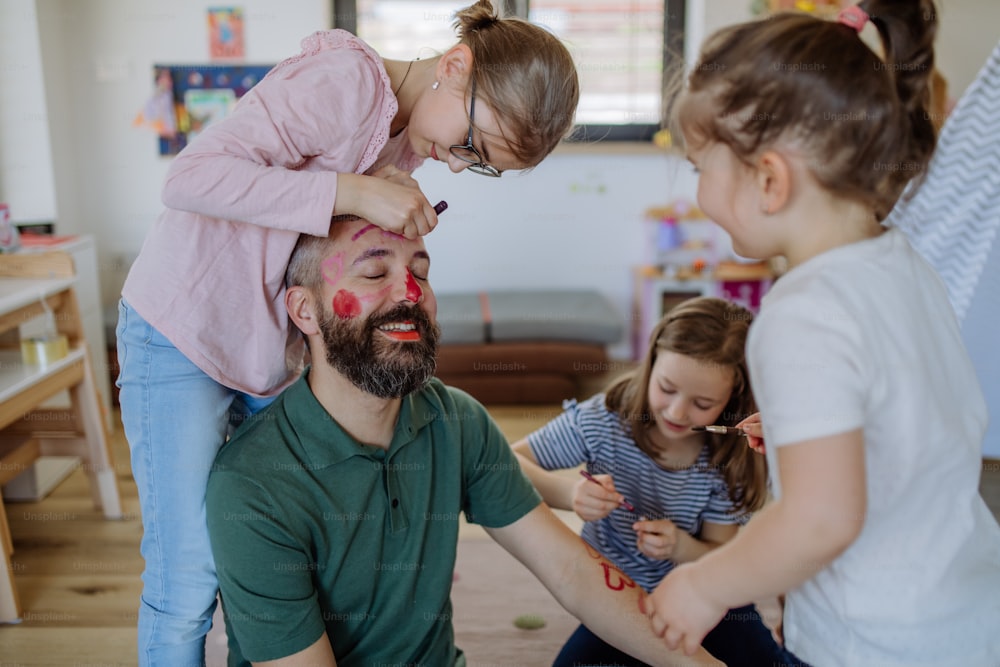 Three little girls putting on make up on their father, a fathers day with daughters at home.