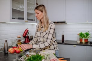 A woman unpacking shopping, vegetables and fruit in kitchen at home.