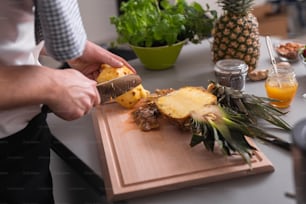 A man standing behind bar counter cutting a pineapple on chopping board.