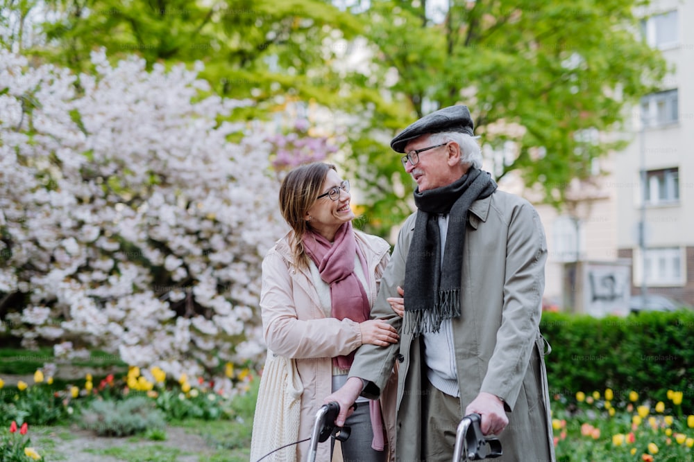 Un uomo anziano con deambulatore e figlia adulta all'aperto su una passeggiata nel parco.