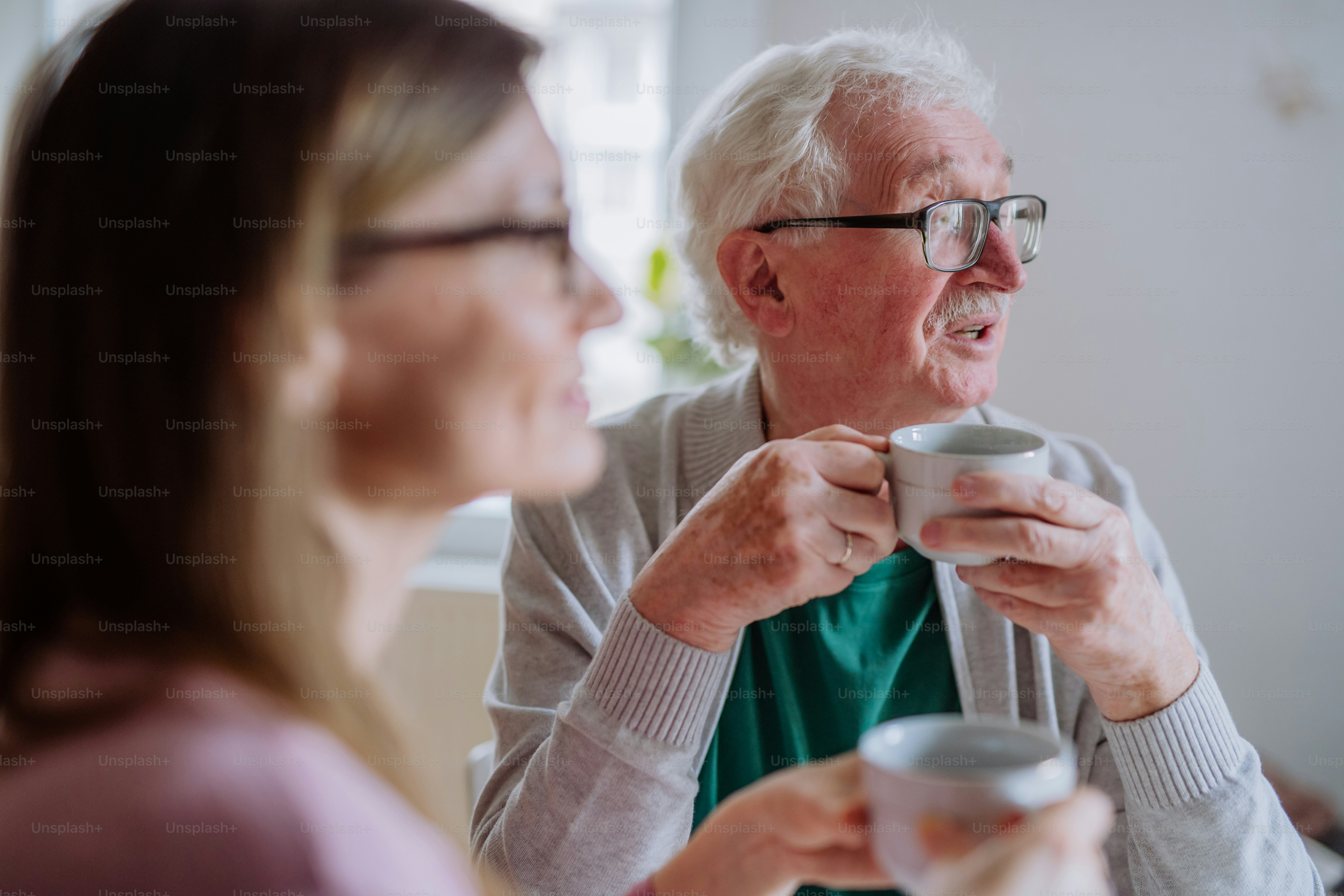 An adult daughter visiting her senior father at home and having coffee together, talking.