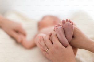 生まれたばかりの赤ん坊の裸足を抱く母親。女性の手の小さな足、接写