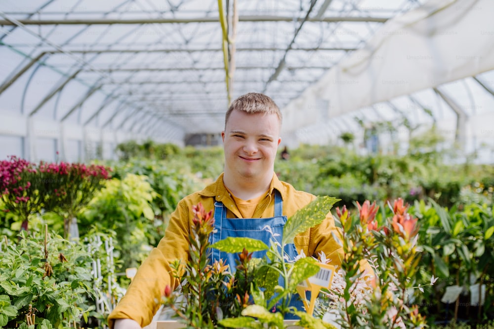 다운 증후군을 앓고있는 청년이 정원 센터에서 일하면서 식물이 담긴 바구니를 들고 있습니다.