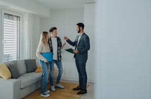 Un jeune couple heureux qui achète sa nouvelle maison et reçoit les clés d’un agent immobilier