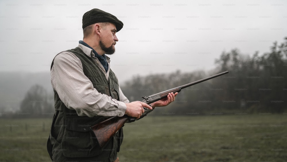 A hunter man in traditional shooting clothes on field aiming with shotgun.