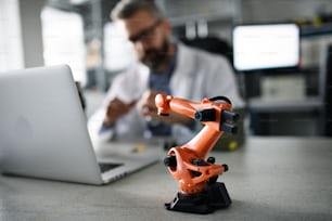 Ein Roboterarm industrielle Miniaturfigur auf dem Tisch vor dem Ingenieur, der im Labor am Laptop arbeitet.