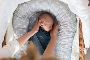 A newborn baby boy sleeping and swaddled in blue cloth lying in grey nest.