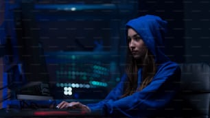 A young woman hacker by computer in the dark room at night, cyberwar concept.