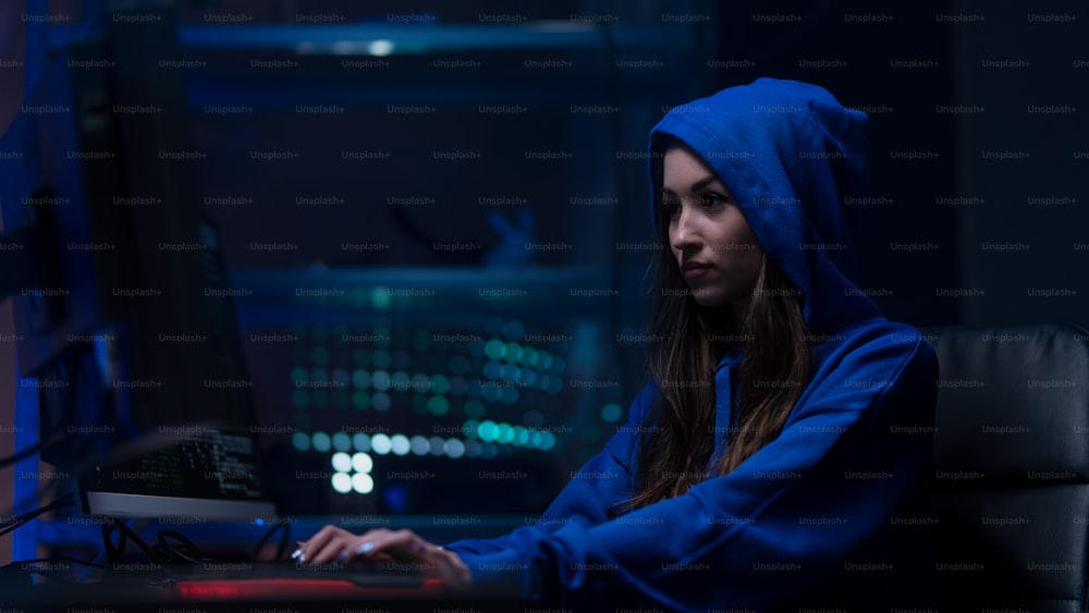 Uma jovem hacker por computador no quarto escuro à noite, conceito de guerra cibernética.