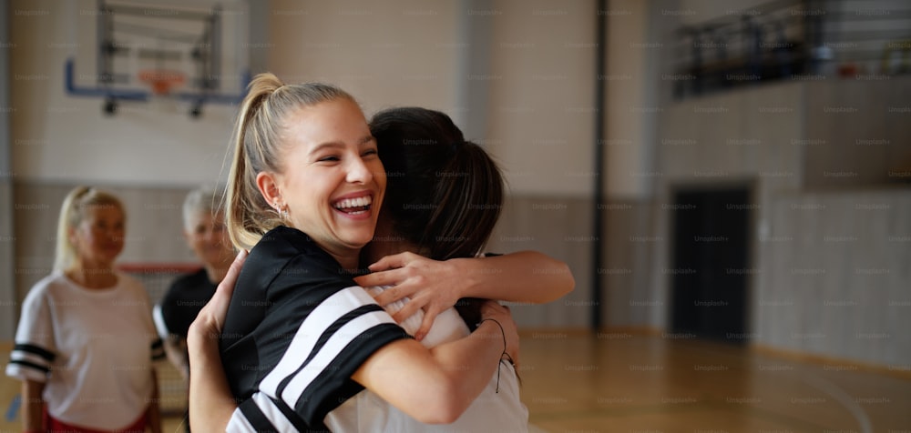 A group of young and old women, sports team players, in gym celebrating victory, hugging.