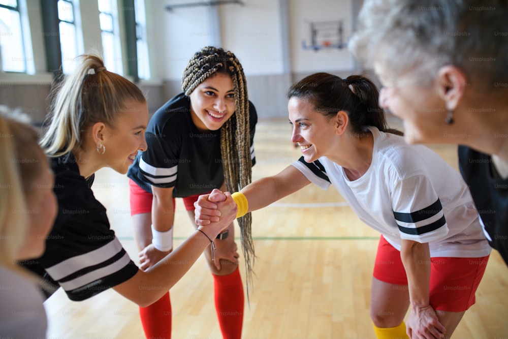 A group of young and old women in gym stacking hands together, sport team players.A group of young and old women together in gym looking at camera, sport team players.
