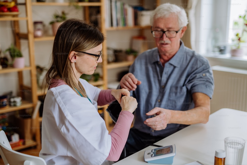 Una dottoressa che visita l'uomo anziano e lo esamina in casa per misurare la pressione sanguigna.