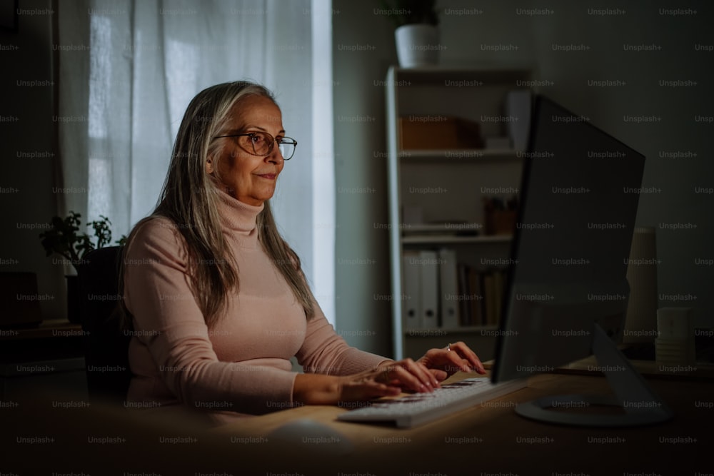 A mature business woman with working on laptop in office at night.
